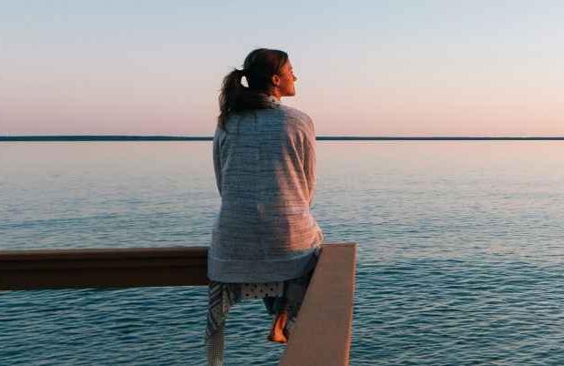 Woman sits on railing by the sea